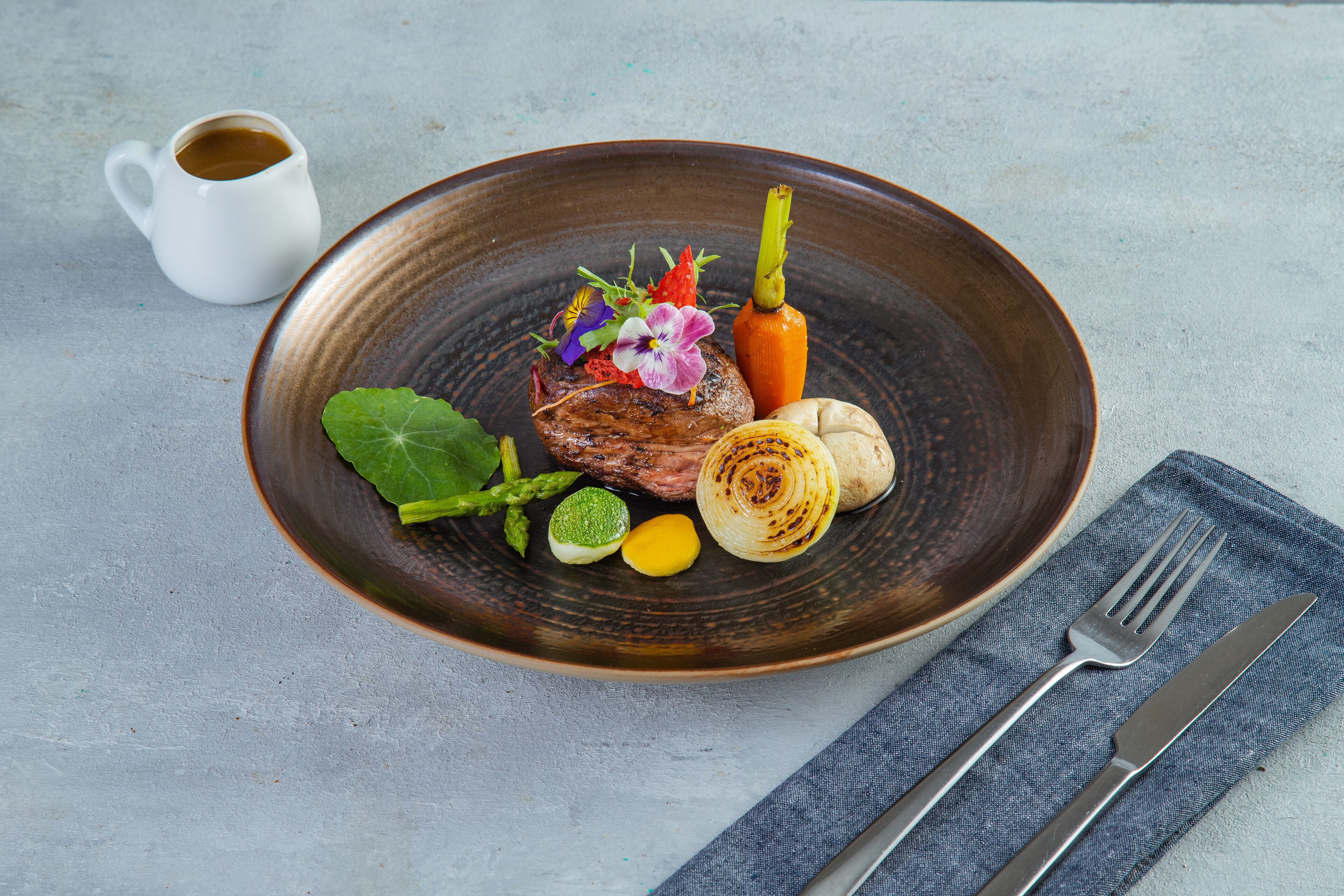 A plate with a steak, vegetables, and a flower garnish.