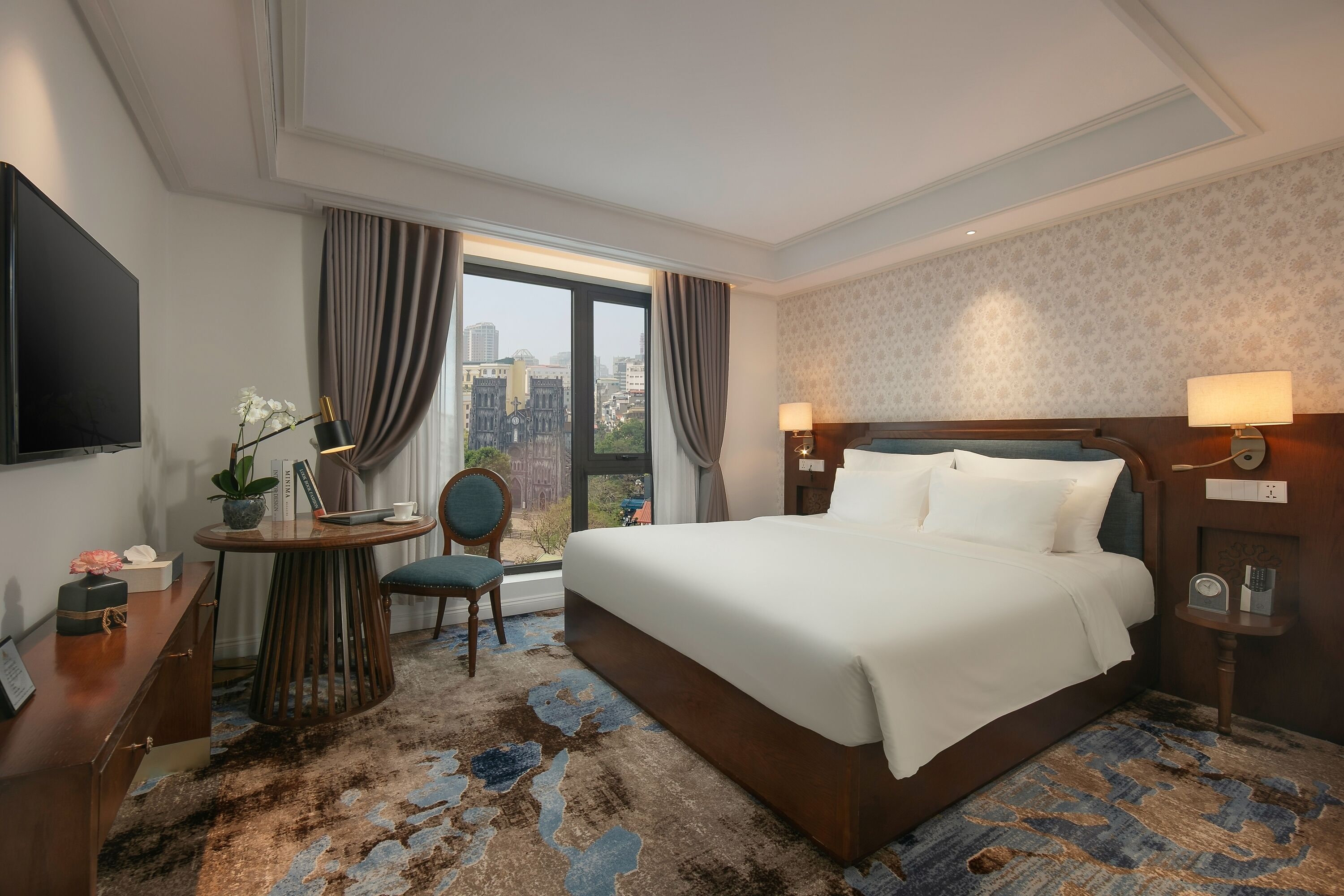 Habitación de hotel con una cama grande, un escritorio con silla, televisión y vista a la ciudad.