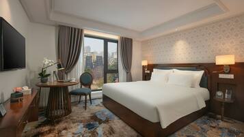 Habitación de hotel con una cama grande, un escritorio con silla, televisión y vista a la ciudad.