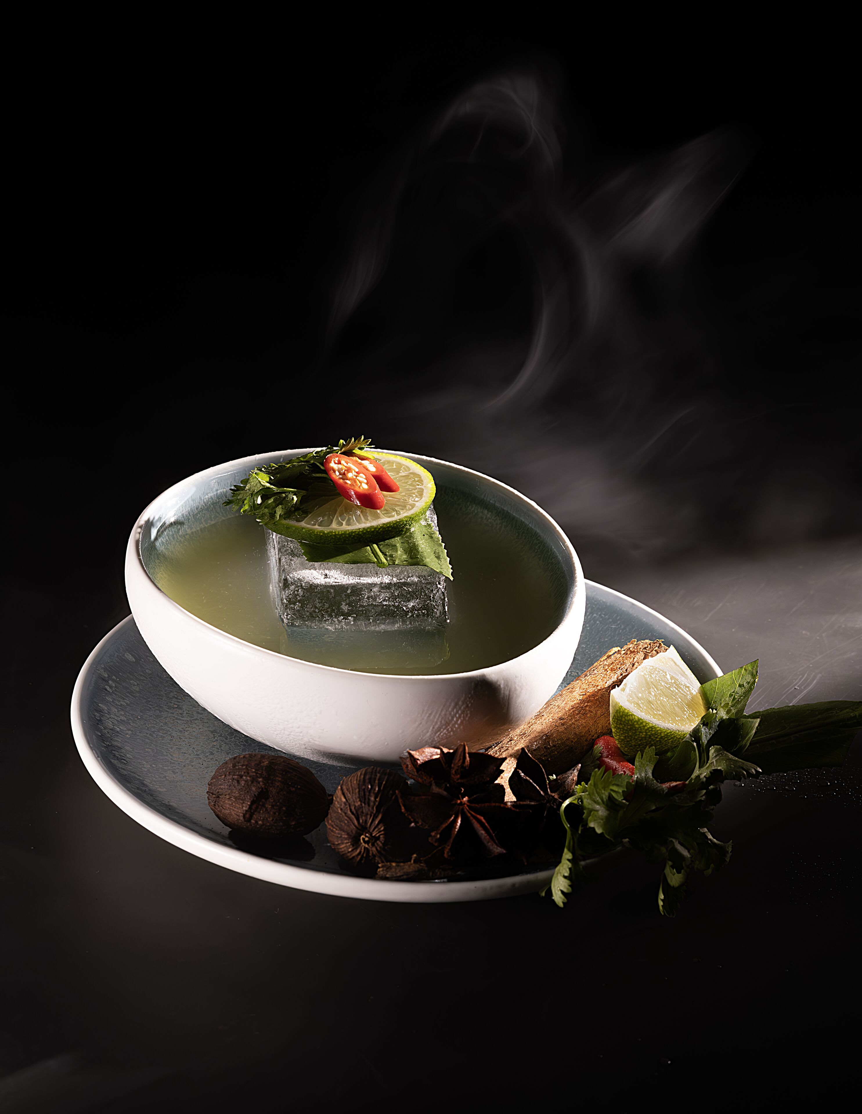 Un bol de soupe, accompagné d’une tranche de citron vert et de quelques piments sur une assiette.
