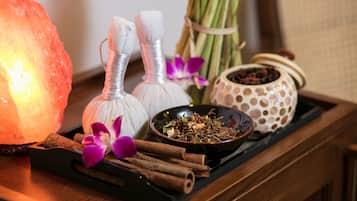 A wooden tray with a Himalayan salt lamp, two white incense burners, a bowl of dried herbs, cinnamon sticks, and a decorative pot.