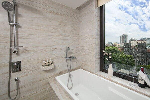 A modern bathroom with a bathtub, shower, and a window with a city view. - The Oriental Jade Hotel (Hanoi)