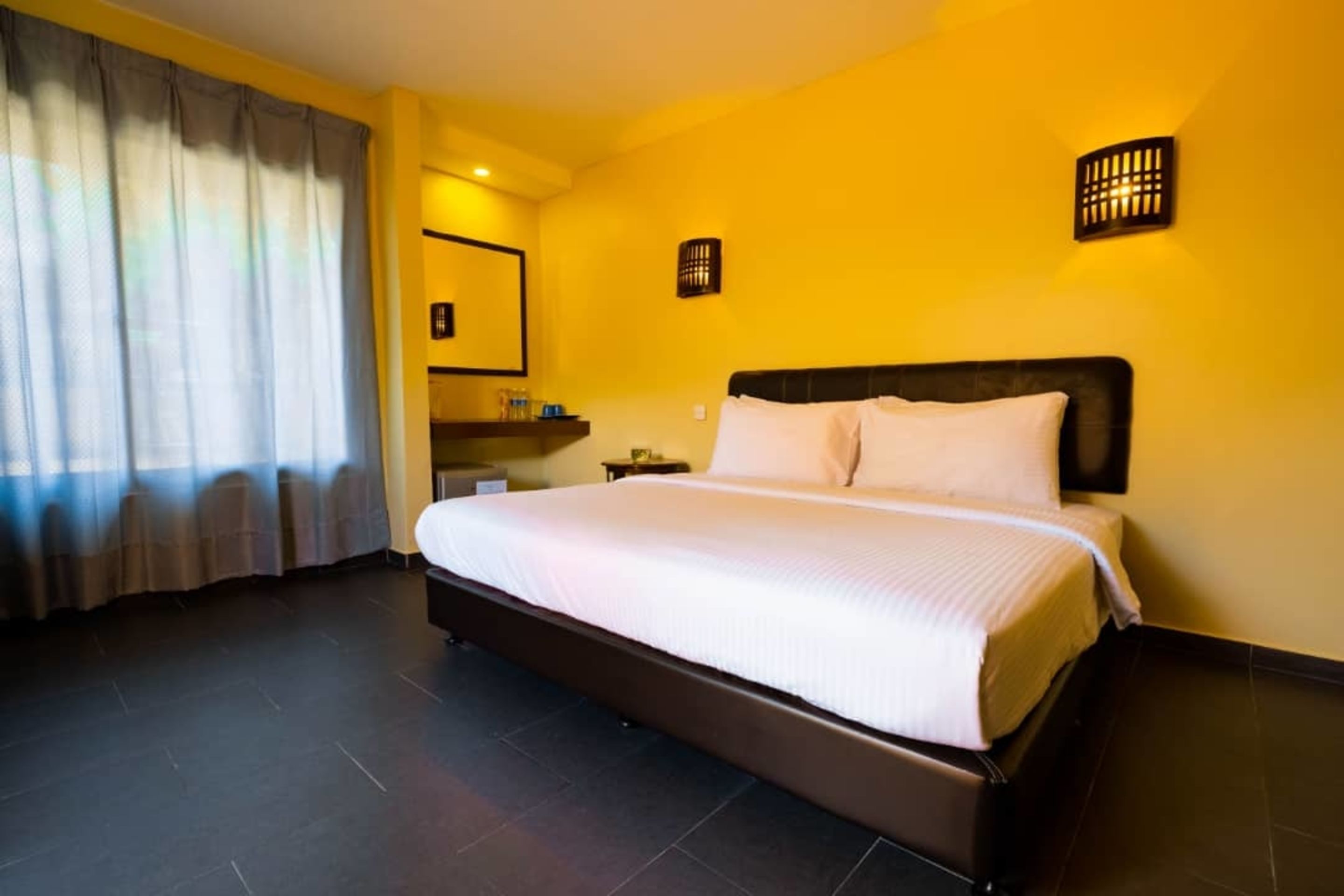 A hotel room with a large bed, a nightstand, a mirror, and a window with curtains.