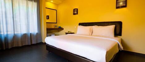 Una habitación de hotel con una cama grande, una mesita de noche, un espejo y una ventana con cortinas.