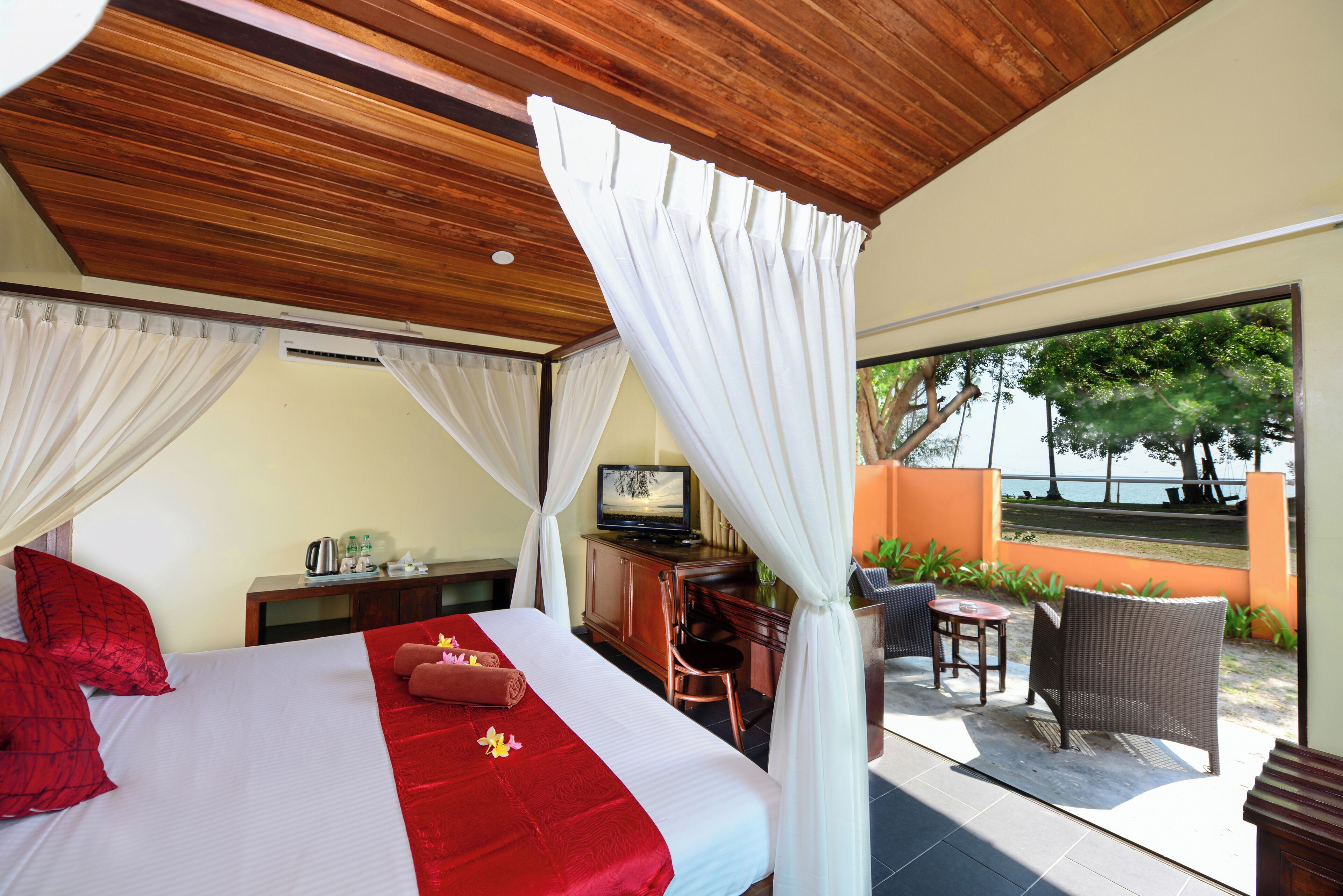 A bedroom with a large bed, a desk with a television, and a view of the outdoors.