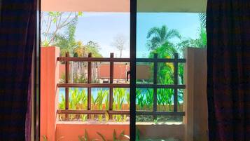 A window with a view of a balcony, plants, and a clear sky.