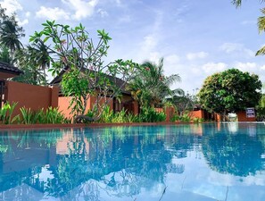 A swimming pool with clear blue water, surrounded by lush greenery and a building with a tiled roof. - Coconut Beach Villa Langkawi (Langkawi)