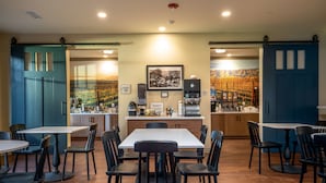 A dining area with a central table and chairs, a coffee machine, and a wall-mounted menu board.