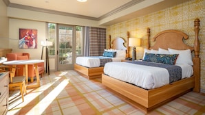 A hotel room with two wooden beds, a desk with a chair, and a large window with curtains.