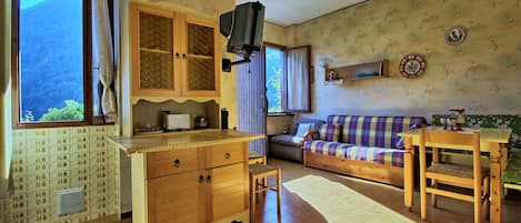 A cozy living room with a sofa, a wooden table, and a kitchen area with a cabinet and a television.