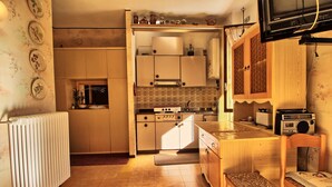 Ett kompakt kök med en inbyggd ugn, en mikrovågsugn och en brödrost. Där finns en trästol och ett litet bord med en radio.