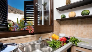 Una cocina con un lavamanos de acero inoxidable, una ventana con persianas, una encimera con verduras frescas y un rebozado de azulejos.