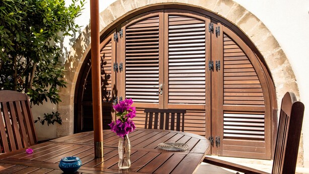 Un área de comedor al aire libre con una mesa de madera, sillas, un florero con flores y un arco de piedra.