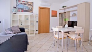 Een woonkamer met een bank, een eettafel met stoelen, een televisie en een boekenkast.