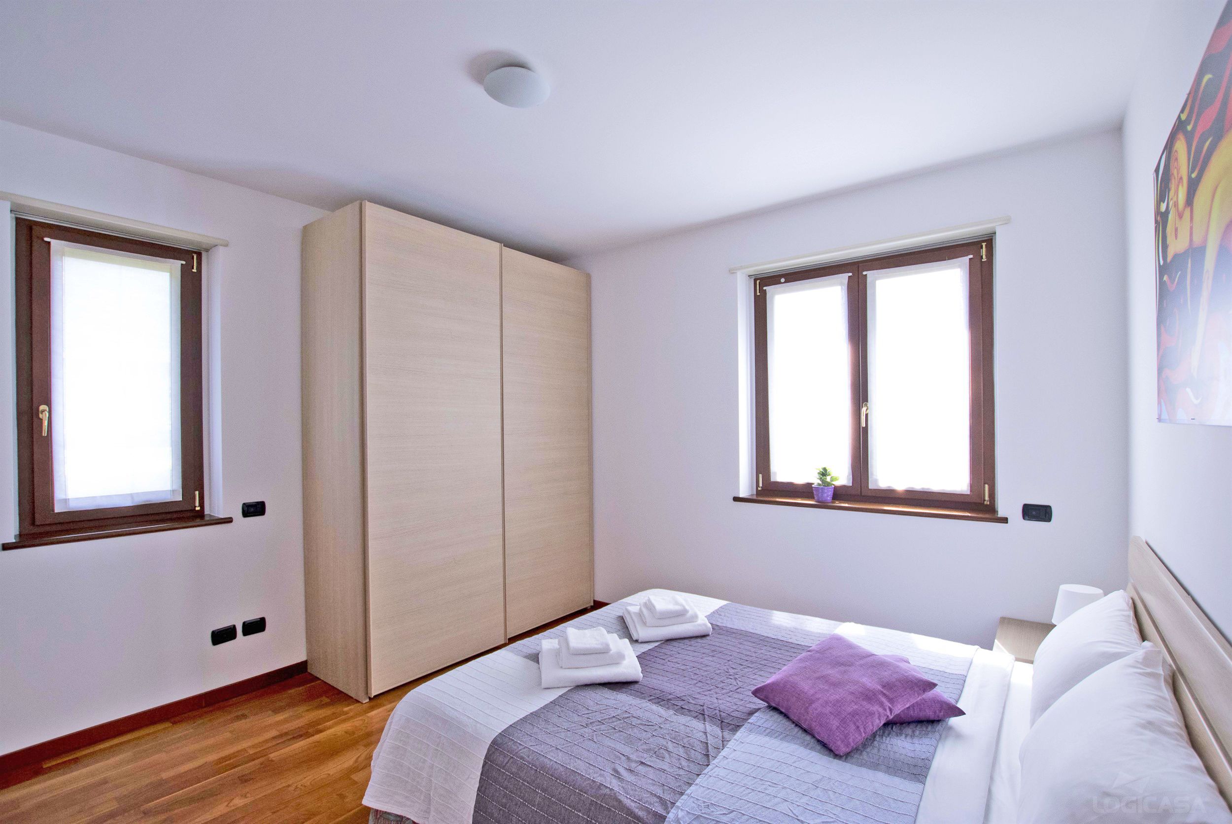 A bedroom with a bed, two windows, a wardrobe, and a ceiling light.