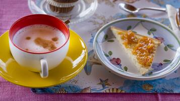 A cup of coffee on a yellow saucer, a slice of orange cake on a floral plate, and a muffin on a glass stand.