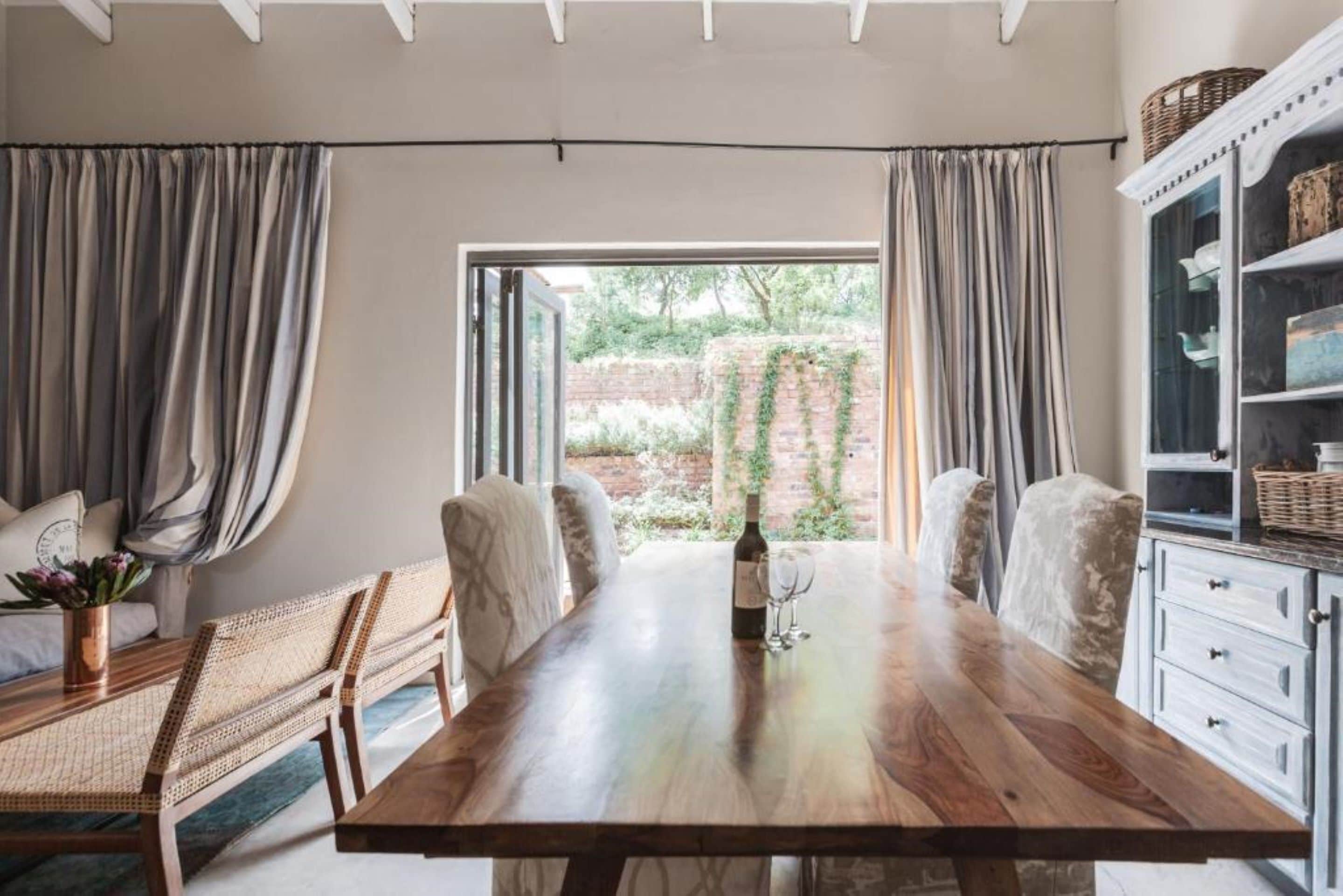 Comedor con una mesa de madera, sillas y vista a un muro de ladrillo y follaje exterior.