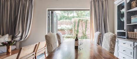 Comedor con una mesa de madera, sillas y vista a un muro de ladrillo y follaje exterior.