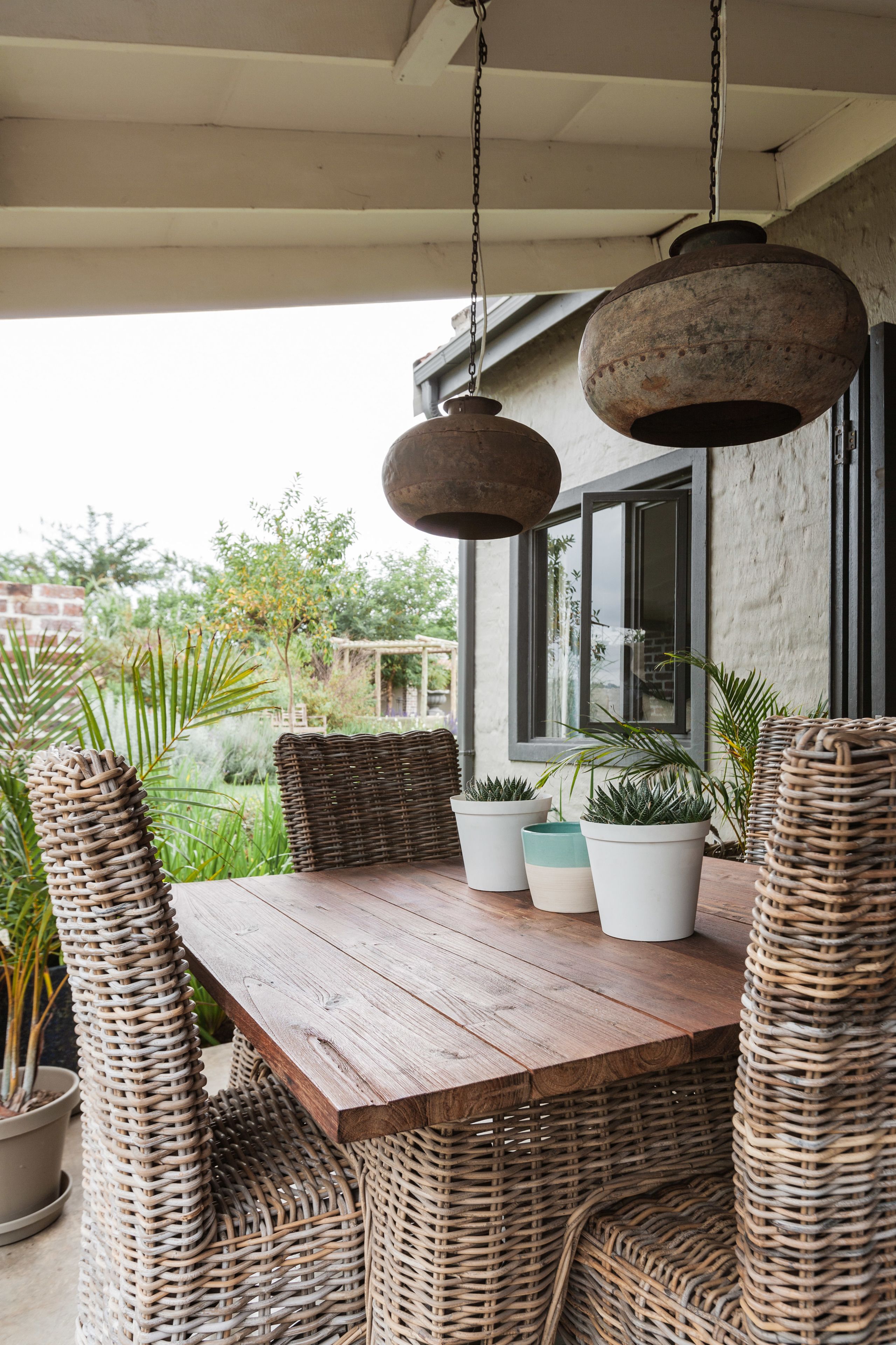 A wooden table with wicker chairs and potted plants.