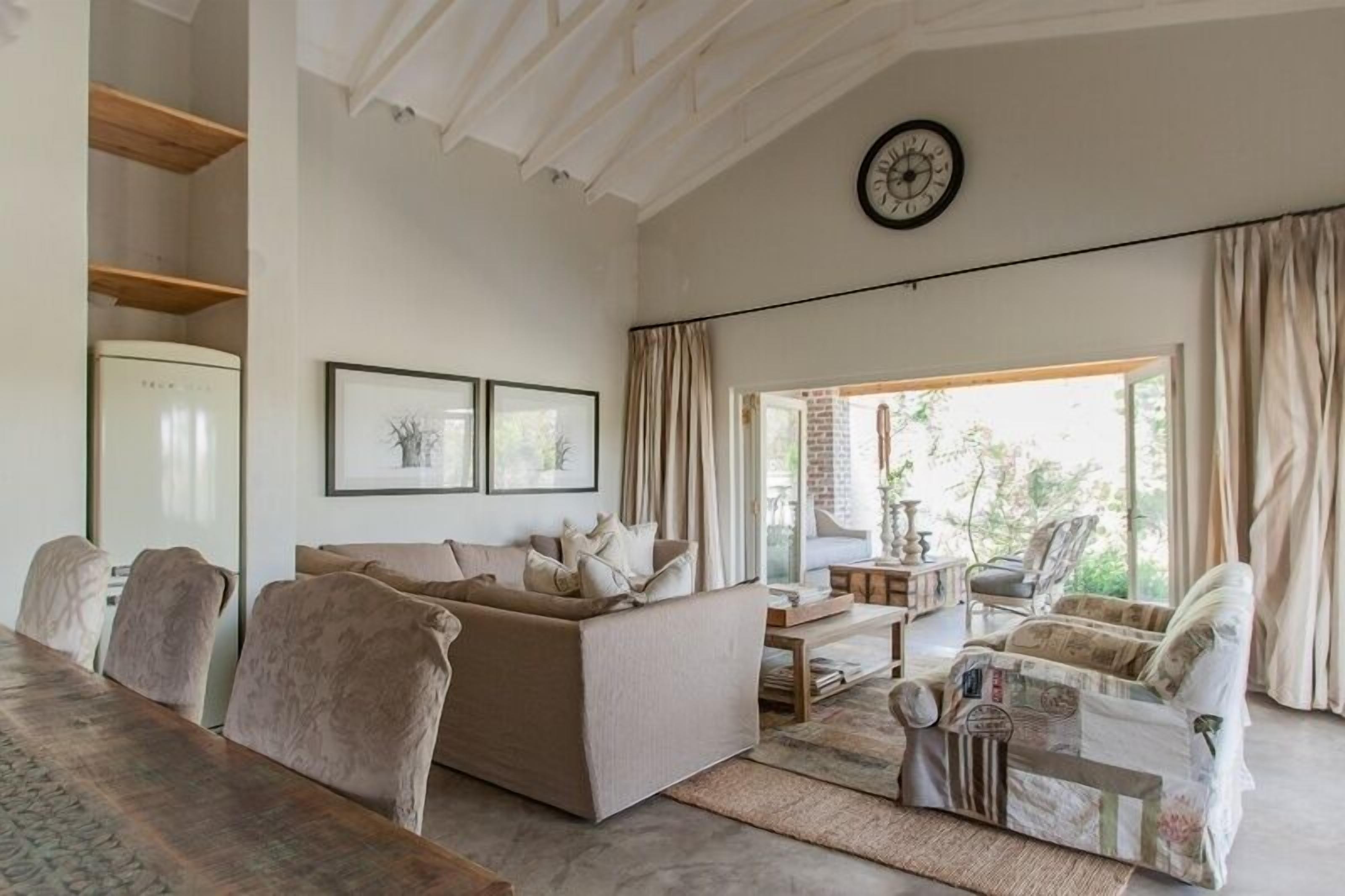 Een woonkamer met een bank, stoelen, een eettafel en een klok aan de muur.