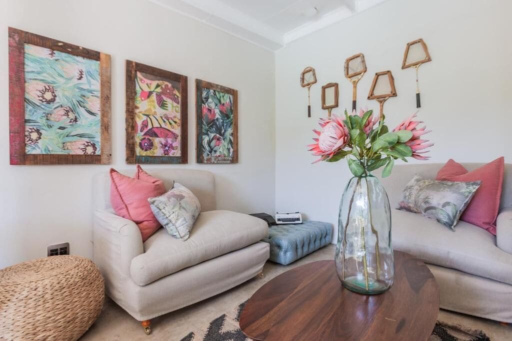 Een woonkamer met twee banken, een salontafel en een vaas met bloemen. Er zijn foto’s in lijsten aan de muur en decoratieve objecten.