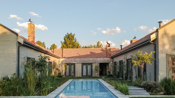A pool with a tiled deck, surrounded by a well-maintained lawn and a brick building with a tiled roof. - Veranda House (Midrand)
