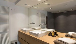A modern bathroom with three white sinks, a large mirror, and a towel rack.