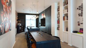 Une cuisine moderne dotée d’un grand îlot central, de luminaires suspendus et d’une bibliothèque remplie de livres.