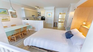 Une chambre d’hôtel comprenant un lit, une table à manger avec des chaises, un coin cuisine et un couloir menant à une autre pièce.