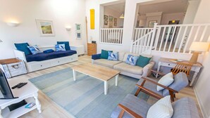 Un salon avec un canapé, une table basse, un téléviseur et un escalier.