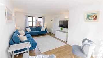 Ein modernes Wohnzimmer mit einem blauen Sofa, einem grauen Sessel, einem weißen Couchtisch und einem Flachbildfernseher.