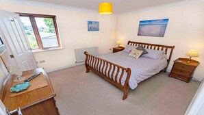 Une chambre à coucher avec un lit en bois, des tables de chevet, une lampe, une fenêtre avec des stores, un radiateur et un tableau au mur.