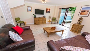 A living room with a brown leather sofa, a wooden coffee table, a television, and a sliding glass door leading to an outdoor area. - Oysters Sleeps 6 Modern Villa & Dog Friendly (Braunton)