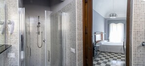 A bathroom with a checkered floor, a shower with a glass door, and a bed with a white bedspread. - Dimora La Torre (Favignana)