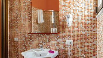 Ein Badezimmer mit einer mosaikverkleideten Wand, einem Waschbecken mit Spiegel darüber und einem an der Wand montierten Föhn.