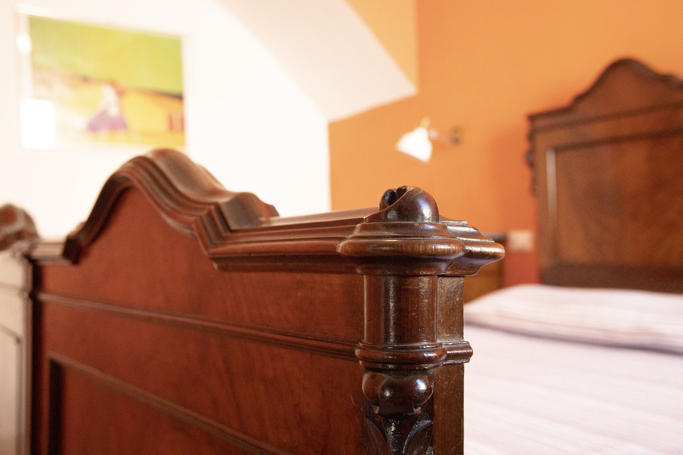 Une tête de lit en bois ornée de sculptures complexes, un lit avec un matelas blanc et un tableau accroché au mur.