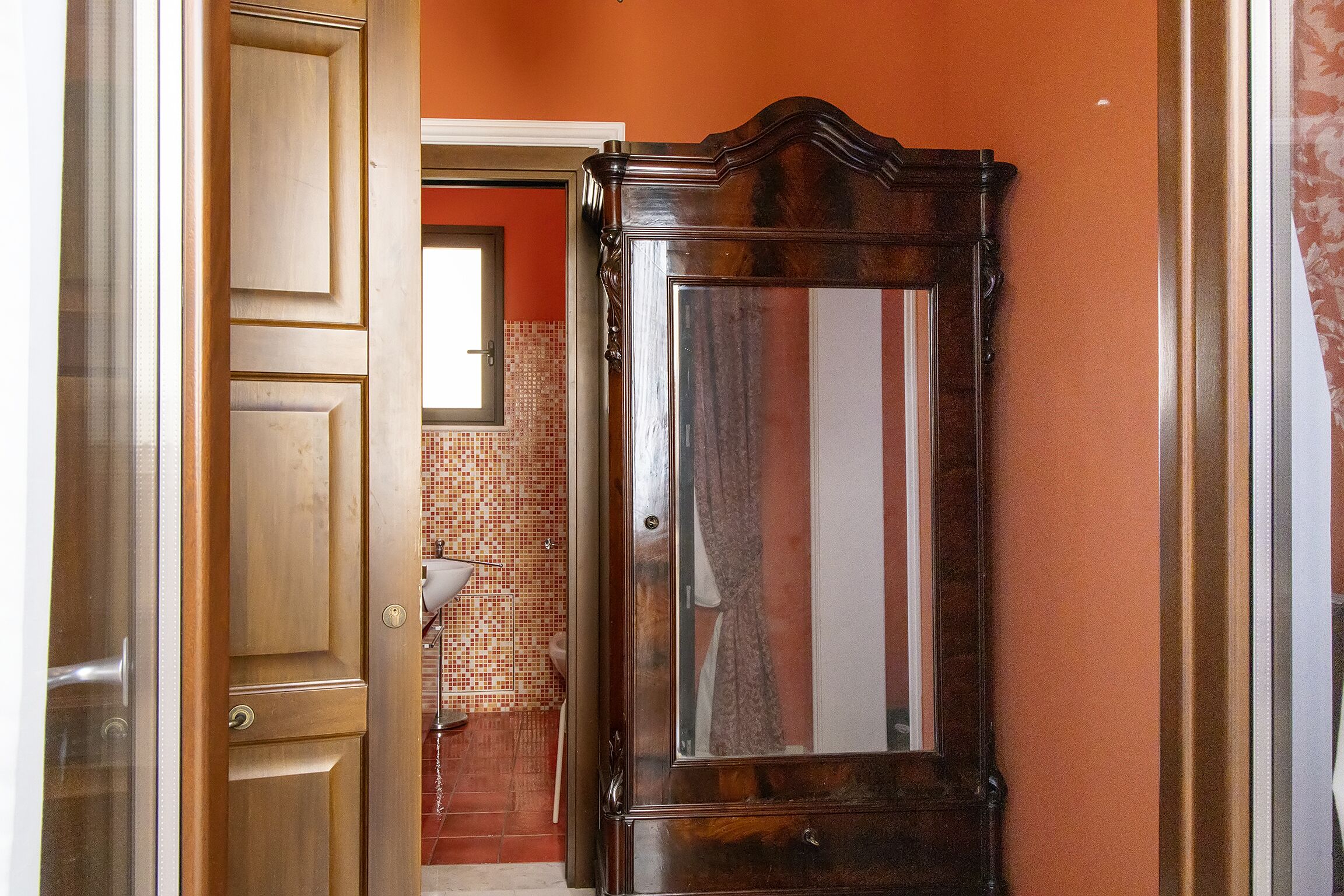 Ein Holzkleiderschrank mit Spiegel, ein gefliester Duschbereich und eine orangefarbene Wand.