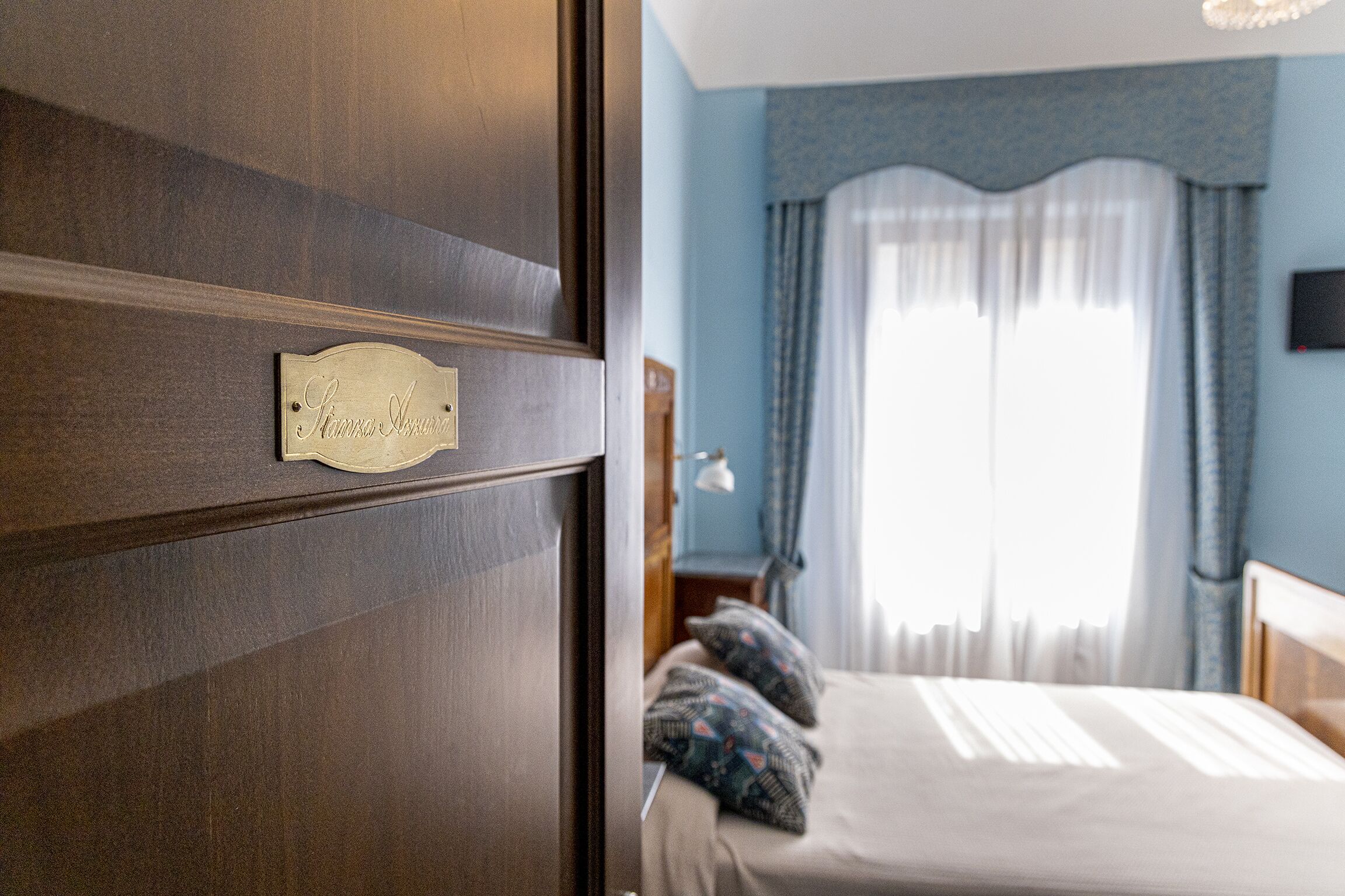 A bedroom with a wooden door, a bed with patterned pillows, and a window with curtains.