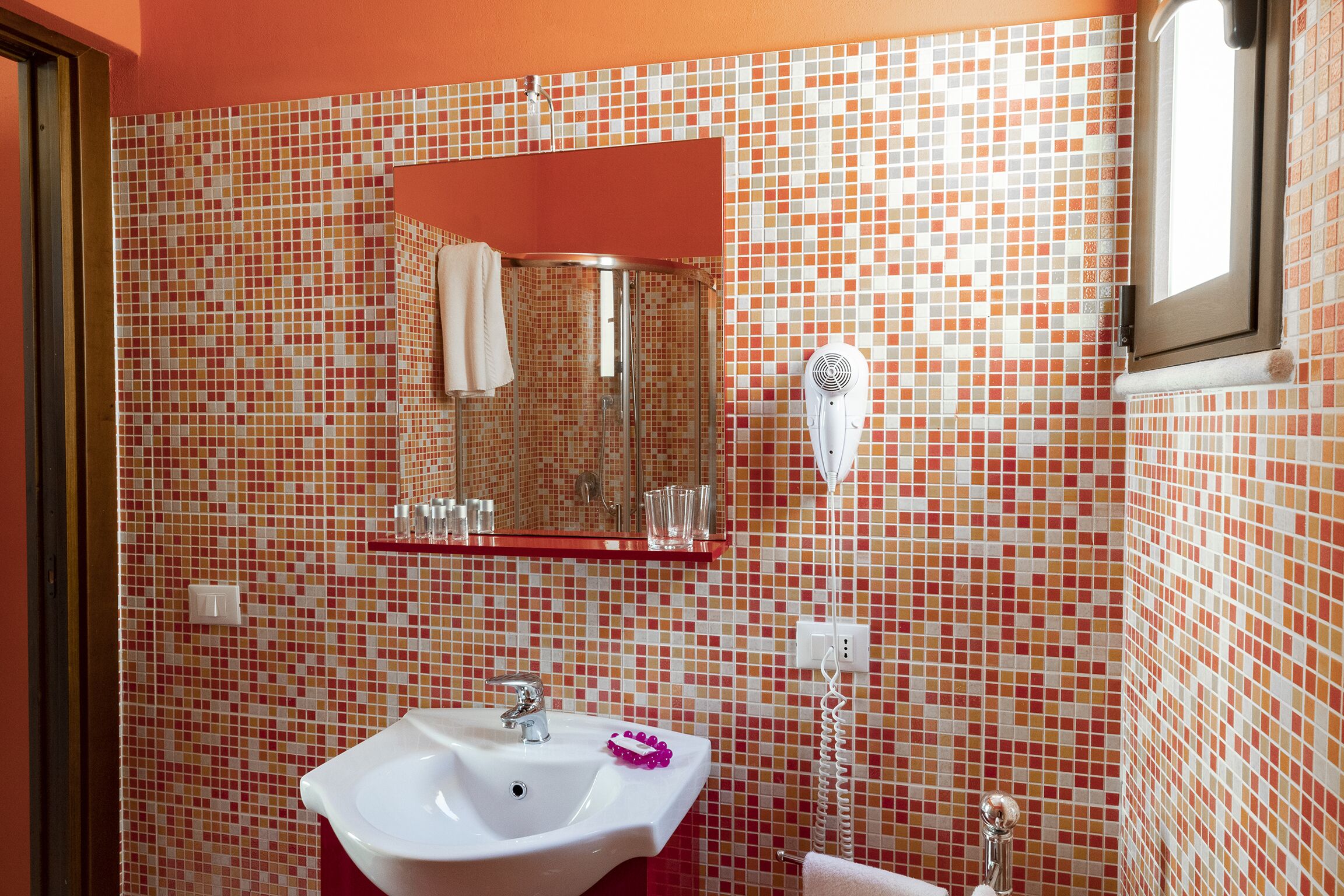 Ein Badezimmer mit einer Wand aus Fliesenmosaik, einem weißen Waschbecken, einem Spiegel und einem Föhn.