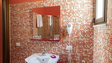 Ein Badezimmer mit einer Wand aus Fliesenmosaik, einem weißen Waschbecken, einem Spiegel und einem Föhn.