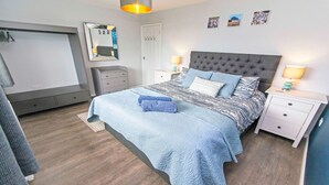 A bedroom with a large bed, two bedside tables, a dresser, a mirror, and a door.