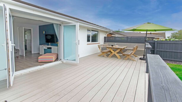 An open patio with a wooden deck, a table with chairs, a bench, and a green umbrella.