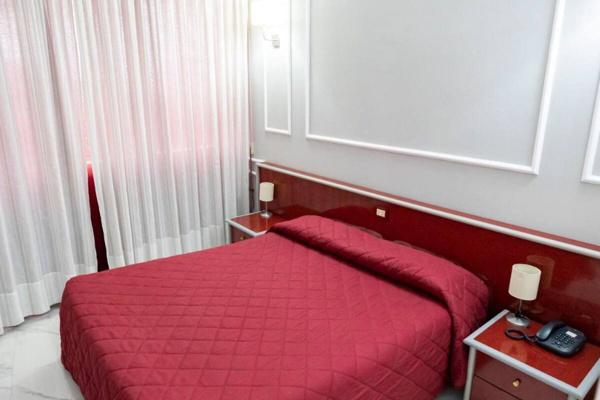 A hotel room with a large bed, a bedside table with a lamp, and a phone.