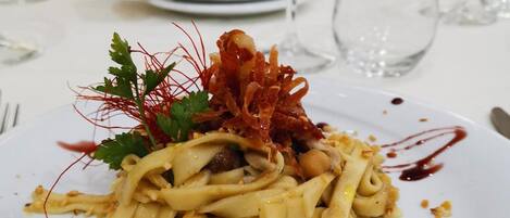 A plated pasta dish with garnishes, accompanied by a white plate and a silver pitcher in the background.