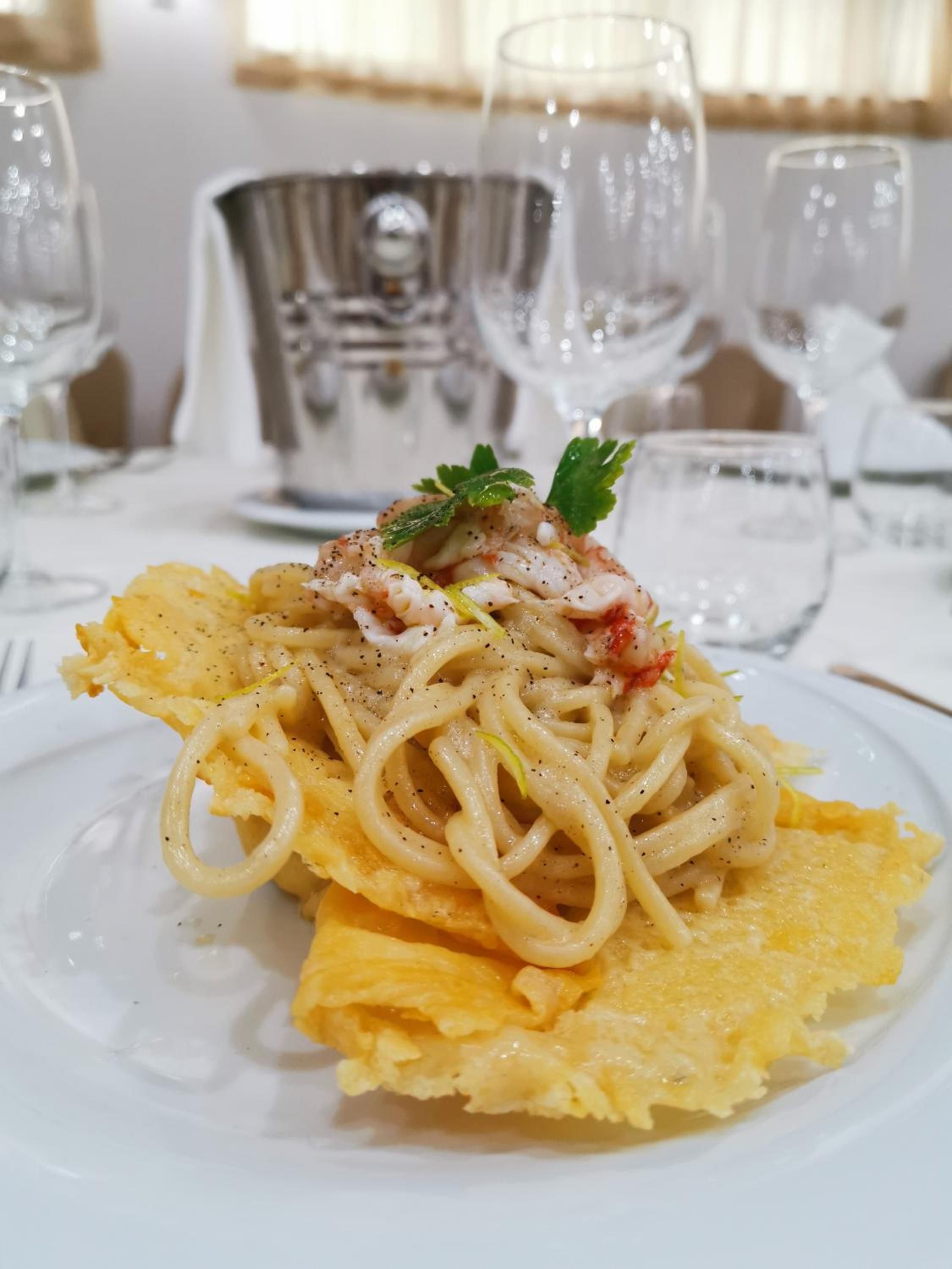 A plate of pasta with a garnish, set on a table with glasses and a silver pitcher.