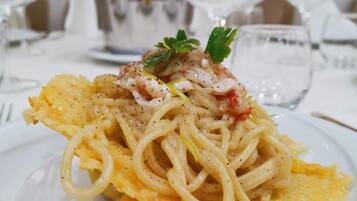 A plate of pasta with a garnish, set on a table with glasses and a silver pitcher.