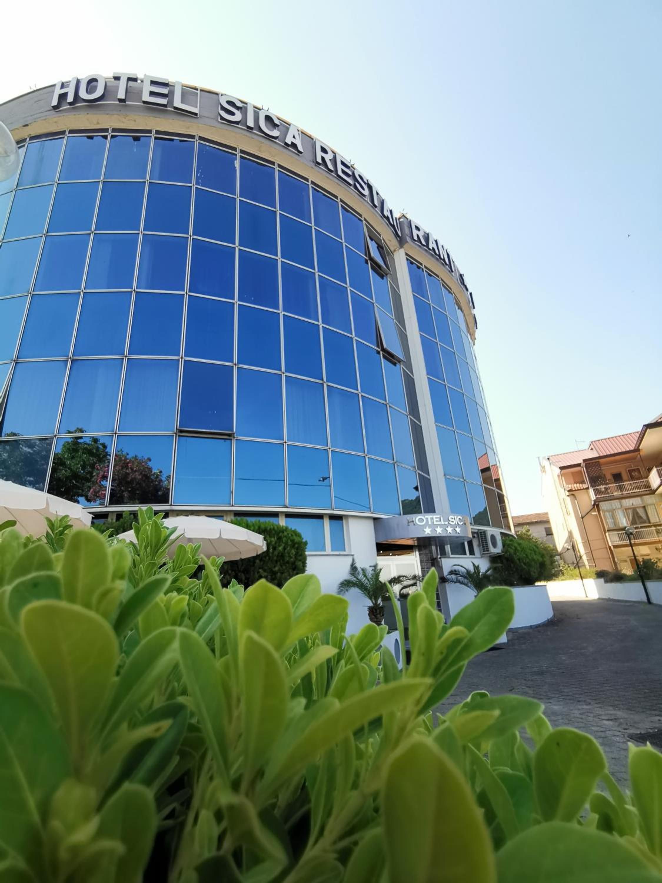 Un moderno edificio de hotel con fachada de vidrio reflectante y un letrero que dice 'HOTEL SICAR RESTAURANT'.