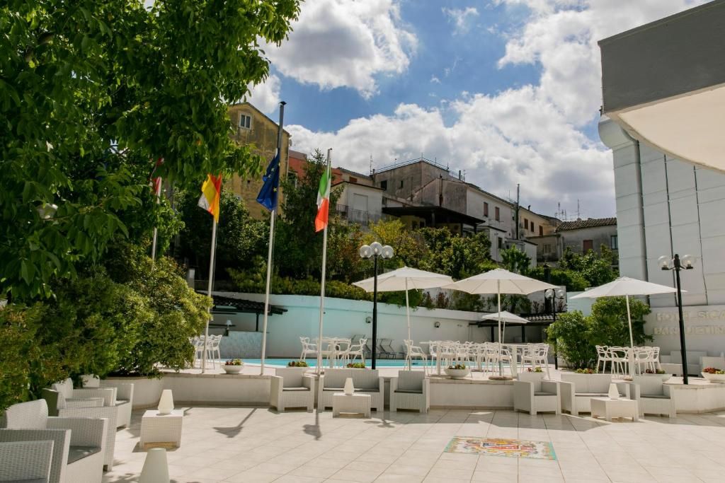 Un área de estar al aire libre con mobiliario blanco, una piscina y banderas.