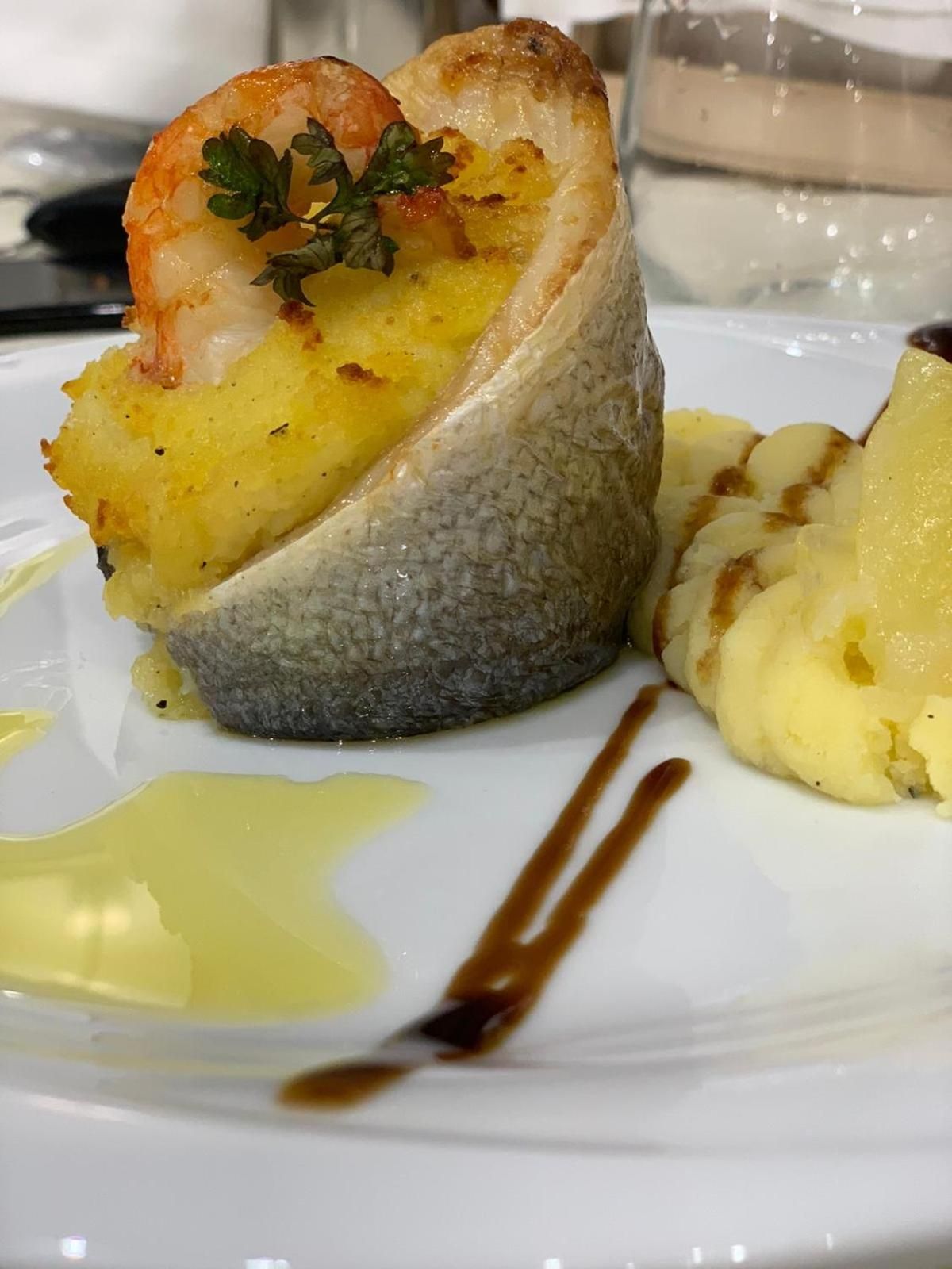 Ein Teller mit einem Fisch-Kartoffel-Gericht, beträufelt mit Sauce.