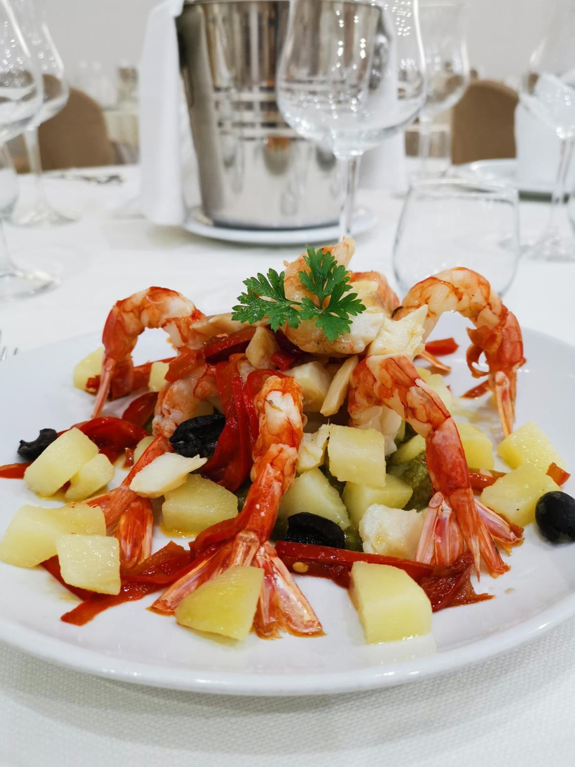Un plato de mariscos con camarones, papas y aceitunas.